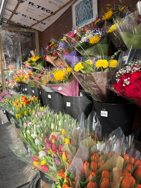 A vibrant display of fresh flowers arranged in bouquets at Harold Wood Station, featuring a variety of blooms including yellow daisies, purple irises, red roses, pink and orange tulips, and mixed gree