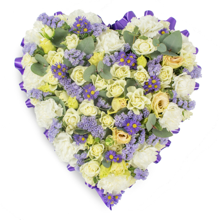 A meticulously composed heart-shaped memorial arrangement, photographed on a stark white background so every texture and tone is clear: the outer edge is precisely traced by a continuous, sumptuous purple satin ribbon that provides a formal, elegant frame. Within that border, pale creams, warm whites and soft yellows dominate-numerous cream and pale yellow roses fill the piece with plush, velvet-like petals, some still in tight bud form, others unfurling to reveal layered centers with faint green undertones. Lush white carnations are layered to add body and a gentle, traditional softness; their ruffled petals create depth and a comforting, familiar feel. Interwoven throughout are clusters of lavender-toned statice whose tiny florets create a delicate, misty texture, and lively, small purple aster-style blooms with bright yellow centers that act as thoughtful accents, catching the eye and offering gentle contrast. Accents of rounded blue-green eucalyptus leaves are scattered across the face of the heart, their matte finish and distinctive shape giving calm structure and a suggestion of clean, aromatic freshness. Soft, even studio lighting highlights the petals' contours and the ribbon's sheen while keeping the mood reverent and peaceful. Designed with sympathy in mind, this heart-shaped tribute would be fitting for funeral services, chapel displays or graveside remembrance in Harold Wood and nearby communities; at Flowers Harold Wood we often craft pieces in this tone to convey dignity, solace and the quiet strength of lasting affection.