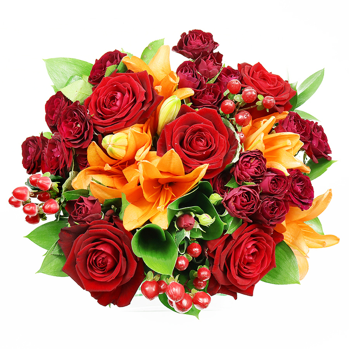 From a bird's-eye view on a clean white background, this sumptuous bouquet presents a layered tableau of deep reds, bright oranges, and fresh greens, arranged with the sure hand of a local florist. Dominant are several fully opened deep red roses, their velvety petals curling back to reveal richly shadowed centres that read as timeless symbols of passion and devotion. Interlaced with these are vivid orange Asiatic lilies; some are wide open with visible stamens and delicate dark speckling, while others hold the promise of bloom in partially unfurled or tight bud forms, lending rhythm and anticipation to the arrangement. Surrounding and filling the gaps are compact clusters of dark red spray roses, their miniature blooms offering a plush, multi-petalled texture that deepens the bouquet's jewel-like quality. Scattered throughout are glossy hypericum berries in bright ruby tones, small spherical highlights that provoke light and contrast against the matte petals. Broad green leaves-likely ruscus or salal-frame the composition and provide a fresh, glossy backdrop that accentuates the warm hues.

Rendered in soft, even light that shows off texture without harsh shadows, the bouquet conveys opulence, warmth, and convivial celebration. It carries the imagined scent of rose depth tempered by the spicy, citrus lift of lilies, and its round, hand-tied form suggests it was arranged for intimate occasions: anniversaries, heartfelt congratulations, or to enliven a living room after a visit to Harold Wood Park or the nearby high street. This design is typical of experienced floristry at Flowers Harold Wood, crafted with attention to balance, seasonal colour, and the tactile pleasures that make a bouquet feel both luxurious and deeply personal.