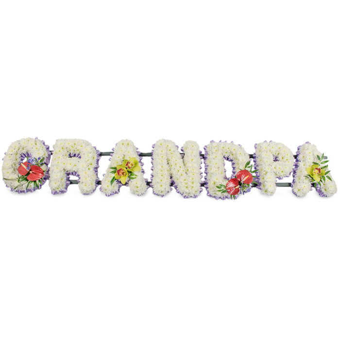 In this photograph, a bespoke floral name tribute presents the word GRANDPA in striking, block-style capitals, arranged horizontally as a single, connected piece. Against the plain white background, the letters appear bold yet soft, each one densely packed with small white chrysanthemums placed so closely together that they form a thick, padded texture resembling a floral cushion. The whiteness of the blooms suggests peace, reverence, and a sense of gentle farewell. At the lower edges of the letters, a narrow line of pale lavender ribbon offers a delicate border, tracing around the base of each shape and adding subtle colour definition. Behind the flowers, a dark green support bar runs steadily, linking every letter and providing structural integrity for display at a funeral service or graveside in Harold Wood. Four tasteful sprays of accent flowers bring life and individuality to the tribute: on the far-left 'G' and the central 'D', clusters of deep red anthuriums emerge, their waxy, heart-shaped spathes and upright yellow spadices framed by glossy foliage and tiny purple filler blooms, creating rich points of visual focus that express deep affection and remembrance. On the first and final 'A', elegant yellow-green orchids flow gracefully over the white chrysanthemum base, their refined petals and soft lime tones adding a contemporary, uplifting touch. The overall impression is one of quiet strength and heartfelt emotion, a floral arrangement that a Harold Wood family might choose to symbolise the love, respect, and gratitude they feel for their grandfather, displayed where family and friends can gather, reflect, and say goodbye.