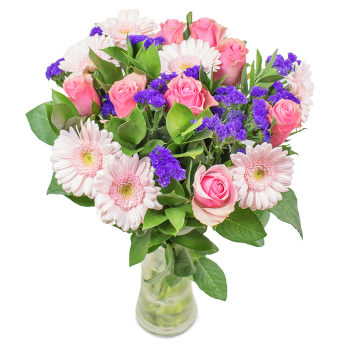 A striking bouquet from Harold Wood, meticulously arranged in a clear glass vase and set against a clean white background, is a celebration of local floral artistry. The arrangement is anchored by approximately eight soft to medium pink roses, their petals swirling in classic spirals-some tightly closed, others just beginning to reveal lavish colour. Interwoven are six or seven pale pink gerbera daisies: broad, radiant blooms with creamy centres that brighten the entire composition. Sprays of vivid purple statice or limonium flowers create lively accents and texture, reminiscent of Harold Wood's vibrant springtime blooms. Lush green foliage underpins the bouquet, enhancing its fullness and imparting a fresh-cut feeling, much like the greenery found walking along Harold Court Road. The transparent vase, with stems visible beneath the waterline, ties the piece together and suggests both freshness and attention to detail. This arrangement, ideal for Mother's Day, birthdays, anniversaries or workplace celebrations in Harold Wood, is designed to convey joy, appreciation, and lasting affection.