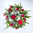 Photographed from directly above against a clean white background, this generous hand-tied bouquet forms a lush, circular pool of colour, as if you were looking straight down into a garden in full bloom on a bright morning in Harold Wood. At the centre, velvety red roses in various stages of opening-some still tight buds, others gently unfurling-create a rich, romantic core. Around them, frilled carnations in deep fuchsia and ruby tones add ruffles, volume, and a playful sense of movement, their petals catching the light with soft shadows. Clusters of small white spray chrysanthemums, daisy-like and cheerful, are tucked between the warmer tones, giving cool highlights that make the reds appear even more vibrant. Sprinkled delicately throughout, tiny white gypsophila blossoms float like a fine mist, softening the edges and lending a dreamy, almost cloudlike texture. Broad, pointed dark green leaves rise between the blooms, likely from lilies or alstroemeria, providing structure and a sense of upward lift. Interwoven with them are rounded, silvery eucalyptus leaves, their muted blue-green shade adding a modern, relaxed elegance and suggesting a fresh, soothing scent. The composition feels full yet carefully balanced, every gap thoughtfully filled, much like a bespoke bouquet prepared for a special birthday or anniversary just off Gubbins Lane. The bright, even lighting and crisp background highlight each stem and petal without distraction, allowing the colours and forms to speak clearly. Altogether, this arrangement radiates joy and affection-as if it has just been finished on the workbench of a local Harold Wood florist, ready for same-day delivery to a loved one's doorstep to celebrate love, appreciation, or a meaningful new chapter.